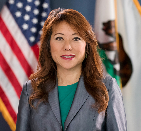 Official portrait of Fiona Ma, California State Treasurer, smiling and wearing a gray suit over a teal dress, positioned between the US and California flags.